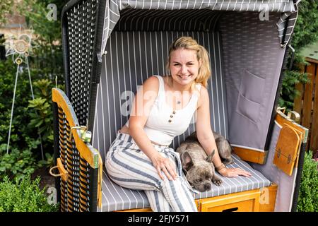 Giovane bionda seduta con il suo cane in proprio sedia da spiaggia in giardino Foto Stock