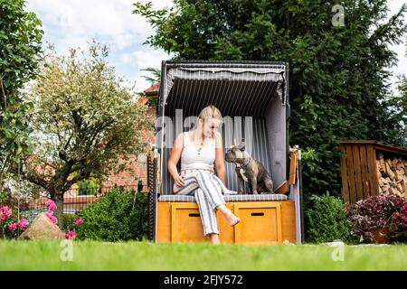 Giovane bionda seduta con il suo cane in proprio sedia da spiaggia in giardino Foto Stock