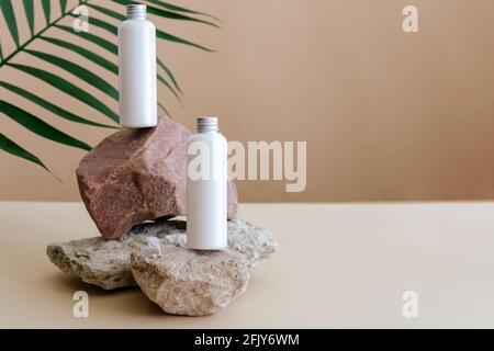 Naturale bellezza bottiglie cosmetiche bianco mockup prodotto cosmetico per la cura della pelle su piedistallo in pietra con foglie di palma. Bottiglie di lozione bianche cosmetiche Foto Stock