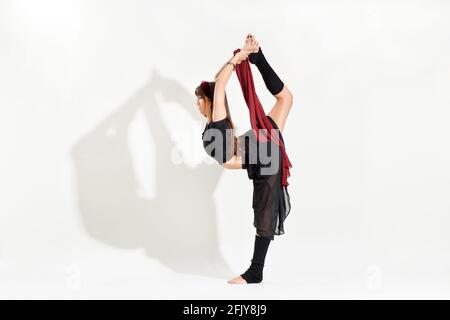 Giovane ballerina che esegue un pattinaggio su ghiaccio Biellman posa allungarsi afferrare il piede mentre si equilibrano su una gamba dentro una vista laterale isolata su bianco con Foto Stock