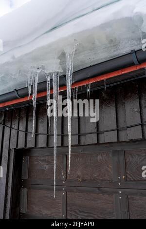 Lunghi icicles pointy da acqua congelata appesa al lato di un tetto. Foto Stock