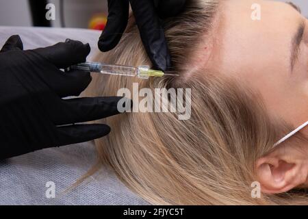 Una donna bionda con capelli tinti soffre di perdita di capelli e riceve iniezioni di mesoterapia nella sua testa. Concetto di restauro dei capelli Foto Stock