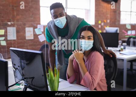 Ritratto di diversi colleghi d'affari che indossano maschere viso brainstorming in parte anteriore del computer Foto Stock