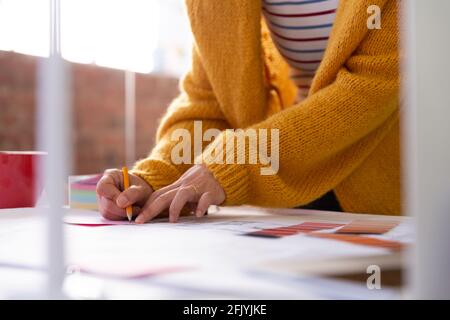 Sezione centrale di donna d'affari in ufficio che scrive e mette le note del memo su blueprint Foto Stock