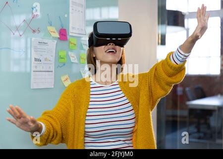 Donna d'affari asiatica sorridente in piedi davanti a lavagna bianca che indossa virtuale cuffie reality Foto Stock