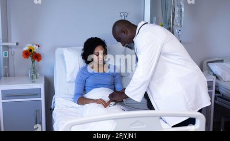 African american maschio medico che mette il pulsossimetro sul dito di paziente misto di razza femminile nel letto Foto Stock