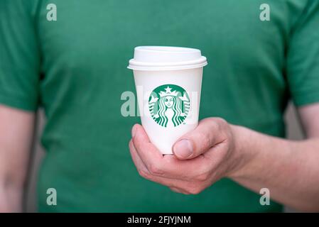 BERLINO - Apr 25: а uomo in T-shirt verde con tazzina di carta bianca e logo Starbucks nel ristorante Starbucks di Berlino, aprile 25. 202 in tedesco Foto Stock