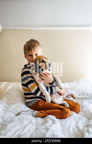 Razze di cane migliori per i capretti, cani di buona famiglia. Presentazione dei cuccioli e dei bambini. Simpatico cucciolo di Beagle e ragazzo che gioca a letto a casa Foto Stock