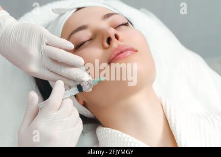 Il dottore cosmetologo rende il ringiovanimento di iniezioni per il viso la procedura di serraggio e levigatura di rughe sulla pelle del viso di una bella Foto Stock