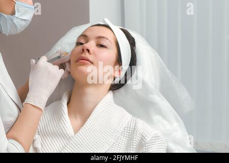 Il dottore cosmetologo rende il ringiovanimento di iniezioni per il viso la procedura di serraggio e levigatura di rughe sulla pelle del viso di una bella Foto Stock