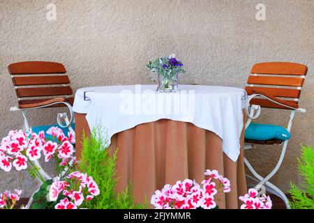 Tavolo con tovaglia per coppia sulla veranda esterna estiva del ristorante. Muro di vecchia pietra testurizzata sullo sfondo. Foto Stock