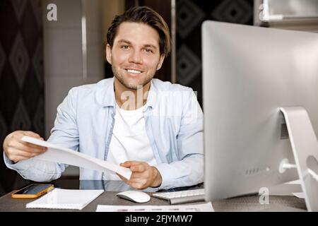 Ritratto di bel freelance maschile è seduto alla scrivania, a distanza di lavoro in ufficio domestico. Uomo d'affari di successo che fa un certo lavoro di ufficio Foto Stock