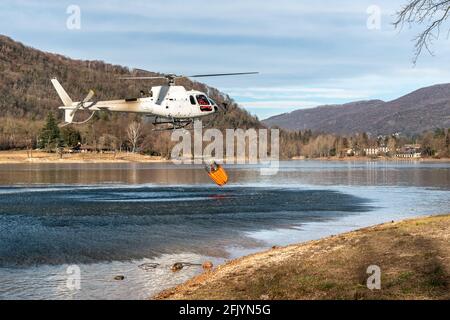 L'elicottero carica acqua dal lago Ghirla per spegnere le fiamme di montagna a Valganna, Italia. La lotta contro gli incendi boschivi. Foto Stock