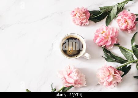 Composizione floreale femminile. Tazza di caffè e fiori di peonie rosa su sfondo bianco del tavolo di marmo. Spazio vuoto. Disposizione piatta, vista dall'alto. Immagine per Foto Stock