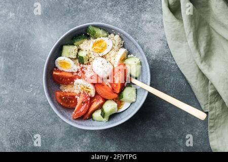 Ciotola per insalata di cous cous vegano con cetriolo, pomodori ciliegini e uova di quaglia su un tavolo di pietra. Foto Stock