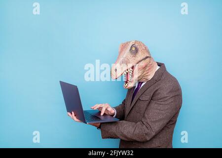 Uomo euforico con testa di lucertola con computer portatile su sfondo blu Foto Stock