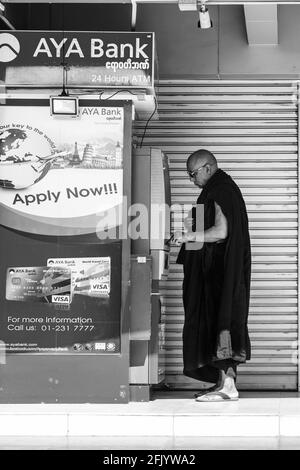 Un monaco buddista ritira denaro da UNA macchina per il cashpoint, Yangon, Myanmar. Foto Stock