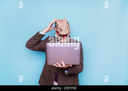 Uomo euforico con testa di lucertola con computer portatile su sfondo blu. Foto Stock