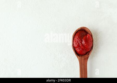 Cucchiaio di legno con pasta di pomodoro su fondo testurizzato bianco Foto Stock