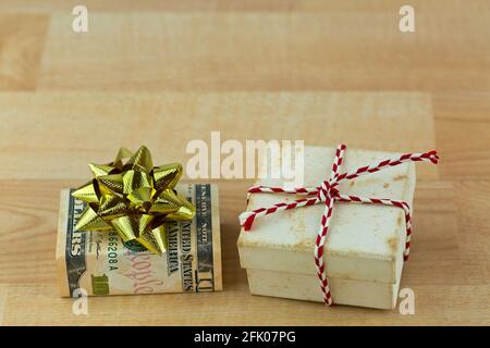Vecchia scatola regalo d'annata arrugginita avvolta con banconote in dollari statunitensi decorate con nastro regalo dorato lucido, scatola presente su woode Foto Stock