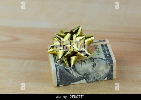 Banconote in dollari statunitensi decorate con un nastro regalo dorato lucido, scatola presente su sfondo di legno Foto Stock