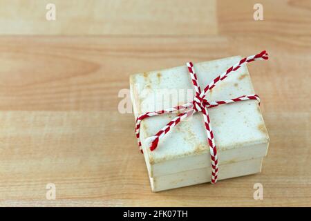 Vecchia scatola regalo d'annata arrugginita con macchie legate corda bianca rossa a strisce su sfondo di legno con copyspace Foto Stock