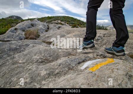 Gambe di un escursionista che cammina nella montagna su un segno del sentiero dipinto nella roccia. Foto Stock