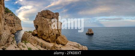 Vista panoramica della vista da una scogliera al tramonto. Con un piccolo isolotto che emerge dal mare Foto Stock