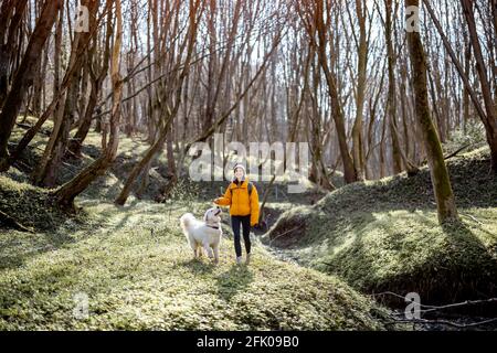 Giovane donna in abiti da trekking e zaino passare il tempo insieme con il grande cane bianco in verde primavera foresta. Gode ed esplora la natura tranquilla. Foto Stock
