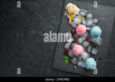 Gelato con ciliegia, mango e cenere di montagna su pezzetti di ghiaccio su fondo nero. Foto Stock