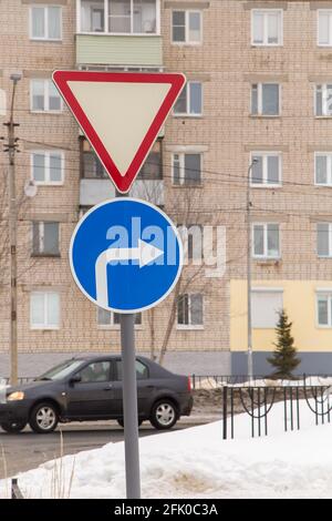 I cartelli stradali significano dare modo e girare a destra solo. Sullo sfondo di una strada e di un edificio residenziale. È inverno in città, la neve bianca si trova sulla strada. Foto Stock