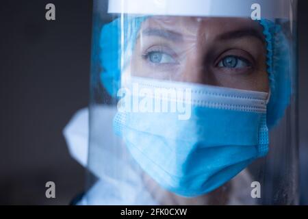 Donna caucasica in ospedale indossare tuta ppe, maschera facciale, visiera e cappuccio medico Foto Stock