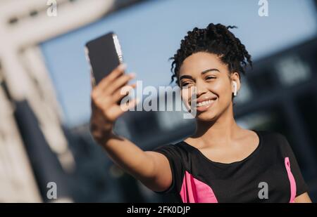 Foto per blog, stile di vita sano e perdita di peso, FIT blog e social network. Sorridente giovane donna afroamericana in abbigliamento sportivo e cuffie prende Foto Stock