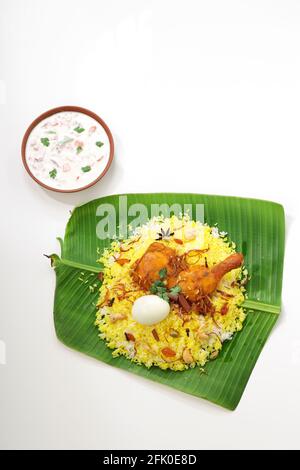 Kerala Pollo dum biryani, disposti tradizionalmente in una foglia di banana e raita come contorno con fondo bianco o consistenza, selettivo messa a fuoco Foto Stock