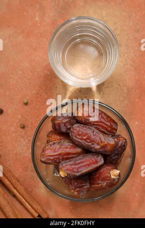 Datteri essiccati, datteri essiccati ramadan messi in una ciotola di vetro con un bicchiere di acqua potabile pura messo su una struttura di legno, fuoco selettivo. Foto Stock