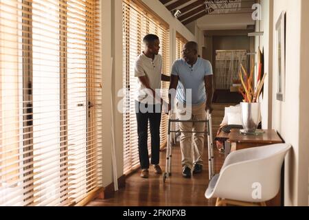 Giovane afro-americano che aiuta suo padre a camminare con passeggio a casa Foto Stock