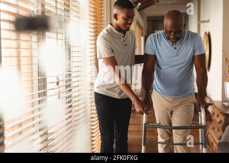 Giovane afro-americano che aiuta suo padre a camminare con passeggio a casa Foto Stock