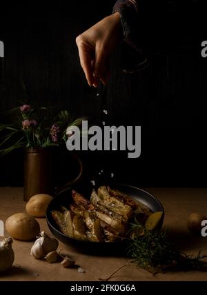 Zeppe di patate su fondo scuro, cottura processo. Processo di preparazione di una ricetta rustica di patate aromatiche al forno Foto Stock