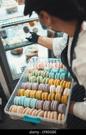 Donna in abito da chef mettendo macaron freschi sul ripiano Foto Stock