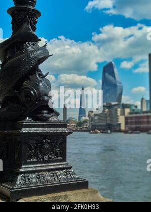 Una vista sul Tamigi da Victoria Embankment, focalizzata su alcuni ornamentali in primo piano in ferro e guardando attraverso i grattacieli della South Bank Foto Stock