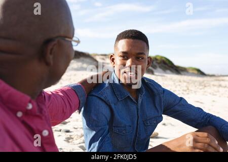 Padre afroamericano che parla con suo figlio mentre sedeva a. la spiaggia Foto Stock