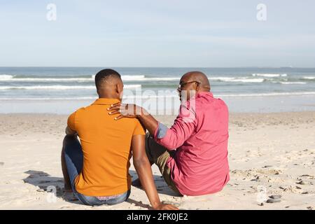 Padre afroamericano che parla con suo figlio mentre sedeva a. la spiaggia Foto Stock