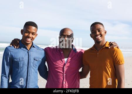 Ritratto del padre afroamericano e dei suoi due figli sorridenti mentre si sta in piedi insieme in spiaggia Foto Stock
