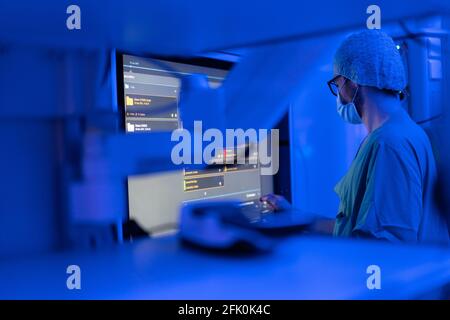 Essen, Germania. 27 Apr 2021. Un'immagine tomografica computerizzata di un cranio facciale è visibile nella sala operatoria ENT dell'ospedale universitario, mentre la luce blu illumina la stanza e un assistente chirurgico cammina attraverso la stanza. Con l'aiuto della luce blu, i vasi sanguigni possono essere visualizzati meglio intraoperatoriamente. La nuova costruzione dell'ala operativa del teatro per le operazioni occhio e ENT costava quasi 70 milioni di euro. Secondo l'Ospedale Universitario, questi sono attualmente i teatri operativi più moderni in Germania e in Europa. Credit: Jonas Güttler/dpa/Alamy Live News Foto Stock