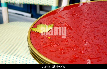 Terrazza del caffè parigino in un giorno d'autunno piovoso. Gocce di pioggia e foglia d'acero sul tavolo. Foto Stock