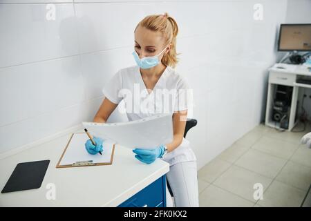 Donna medic su una sedia che annotano giù i particolari di radiografia Foto Stock