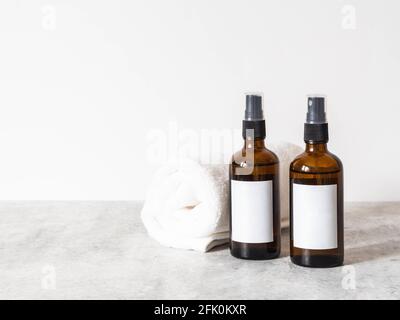 Due bottiglie di vetro marrone con etichetta bianca e asciugamano bianco su tavolo grigio in bagno. Vista frontale. Spazio di copia. Blogging concetto minimo di bellezza, cosmetici Foto Stock