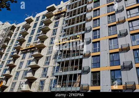 Edificio moderno in costruzione contro il cielo blu. Costruttori professionisti che lavorano in culle sulla facciata di una casa residenziale a più piani Foto Stock