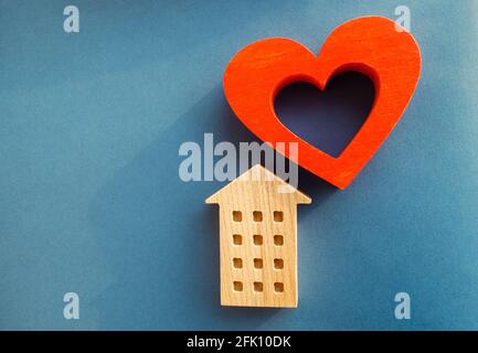 Casa di legno e cuore rosso su sfondo blu. Concetto di casa dolce. Assicurazione sulla proprietà. Una nuova casa per la famiglia. Comfort familiare. Ipoteca acquistabile Foto Stock