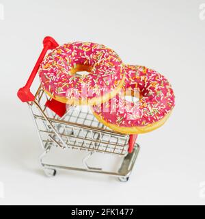 Due ciambelle rosa smaltate in carrello giocattolo da vicino supermercato. Vendita, acquisto, consegna di prodotti freschi da forno, negozio online e alimenti malsani Foto Stock